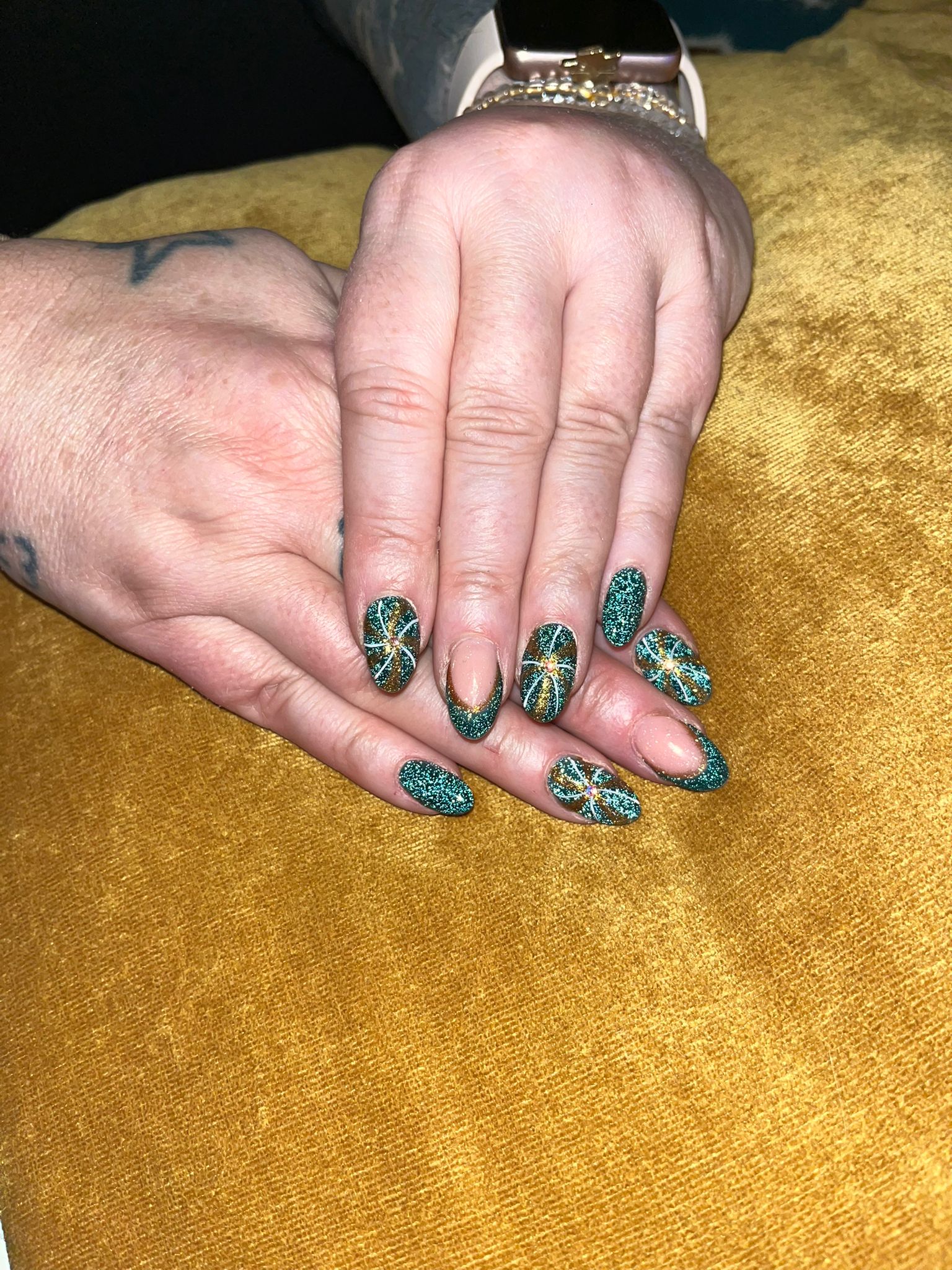 Groene glitternagels met gouden lijntjes op een okergele fluwelen ondergrond
