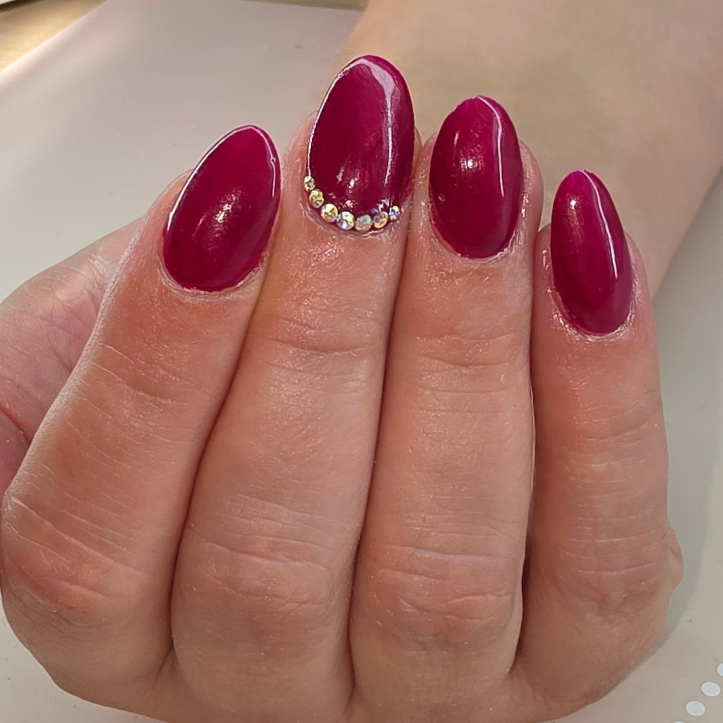 Bordeauxrode nagels met een rij steentjes op de ringvinger