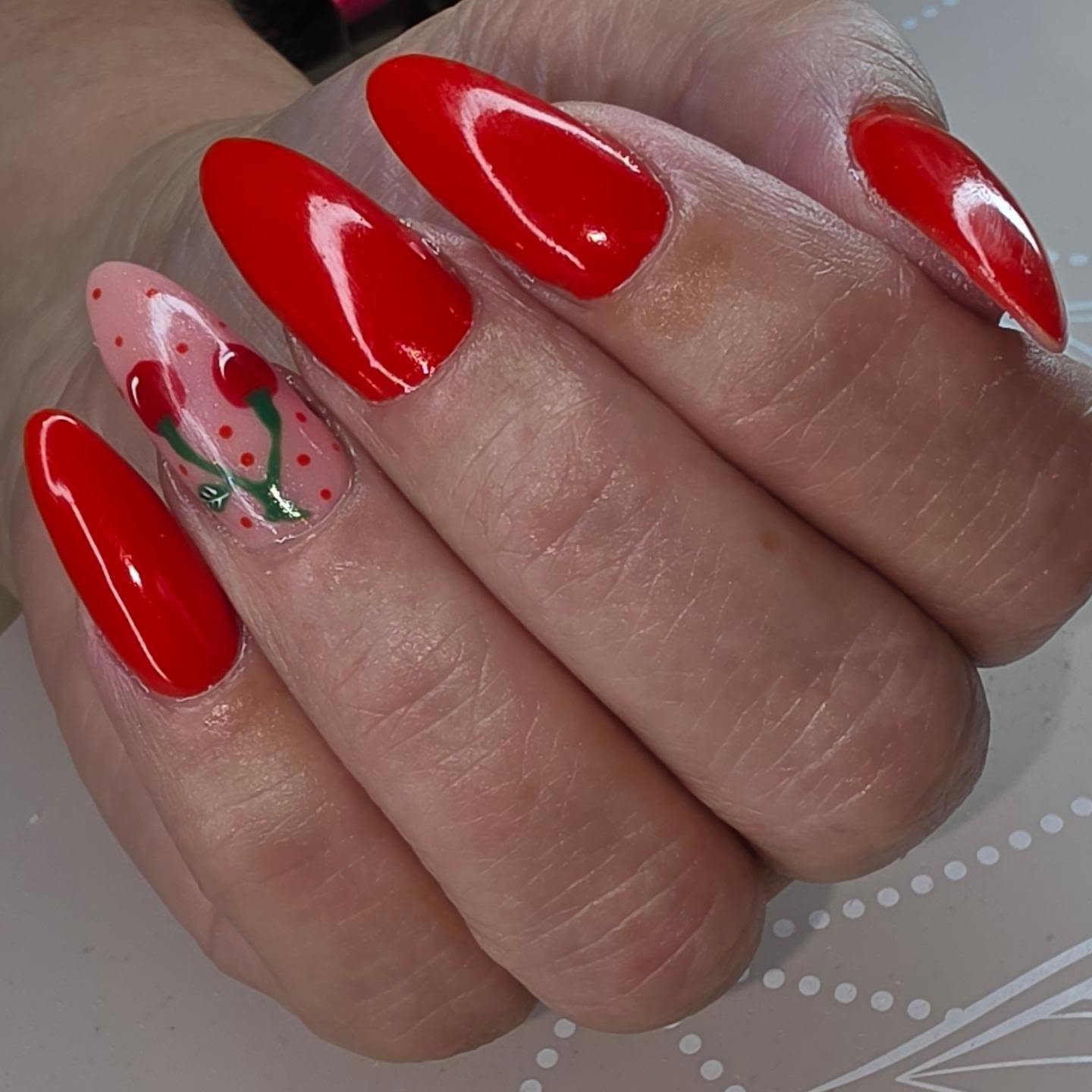 Felrode amandelnagels met een kersjesmotief op een roze nagel