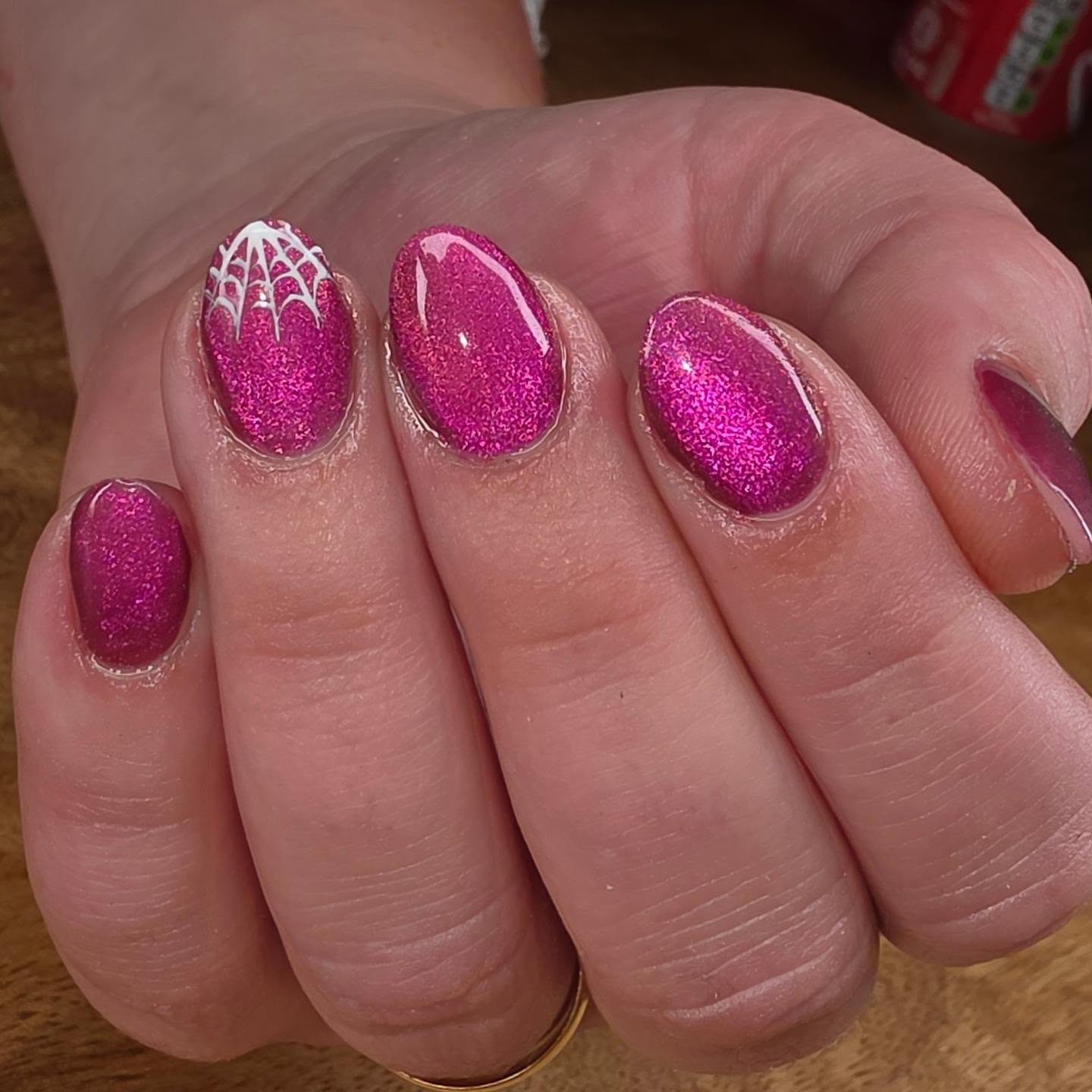 Roze glitternagels met een wit spinnenweb op de duim